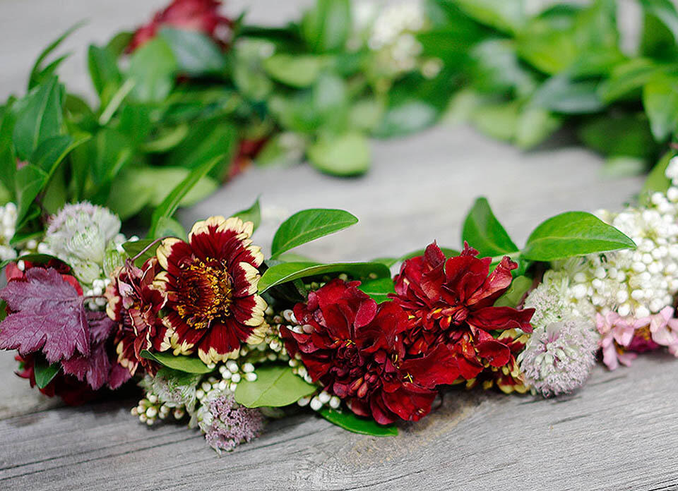 Färdig krans i grönt och rött med bland annat vintergröna, tagetes och zinnia.